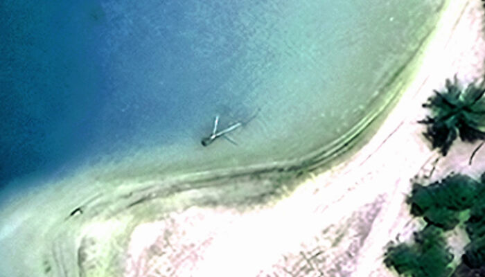 Aerial view of a shoreline with a large object partially submerged in water, related to Amelia Earhart mystery.