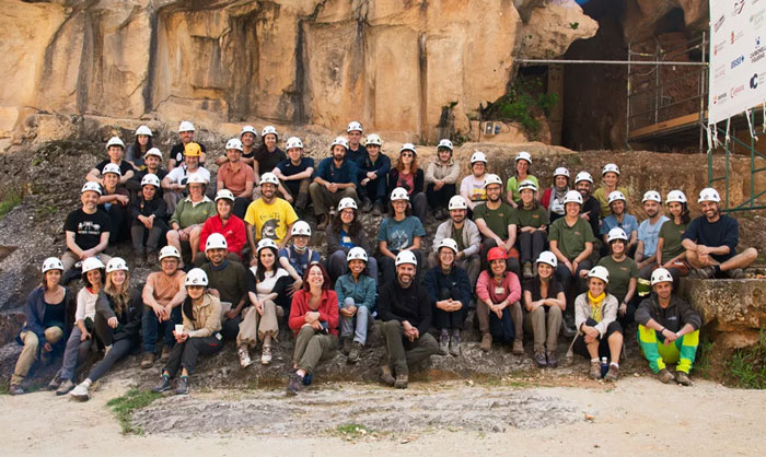 Group of archaeologists wearing helmets posing together at a prehistoric site linked to toddler prey evidence discovery.