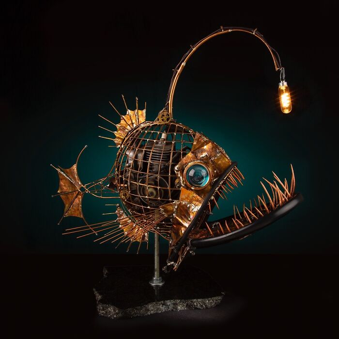 Fish sculpture made from scrap metal with intricate details and a glowing light bulb as a lure, showcasing striking animal sculptures.