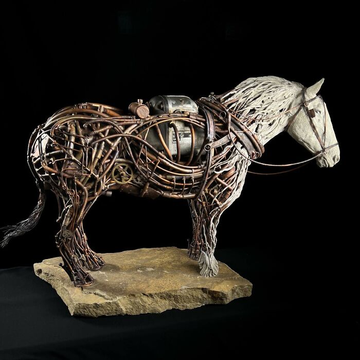 Horse sculpture made from scrap metal showcasing intricate animal sculpture details on a stone base against black background.