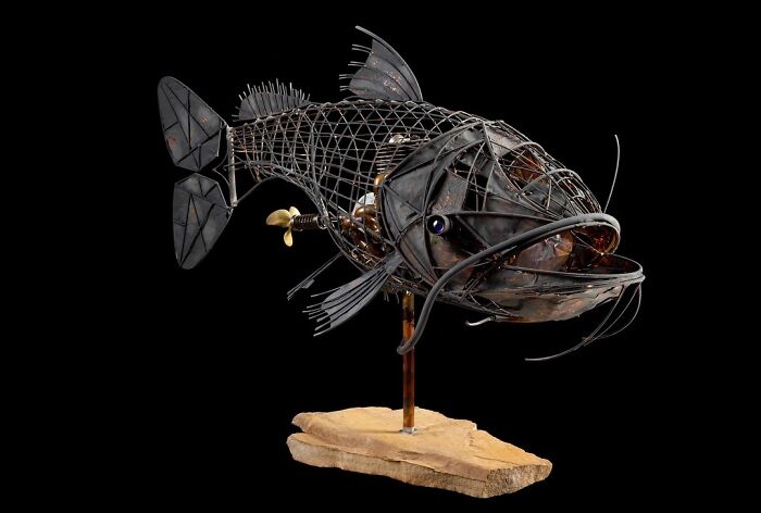 Scrap metal animal sculpture of a fish with intricate wire and metal detailing mounted on a wooden base.