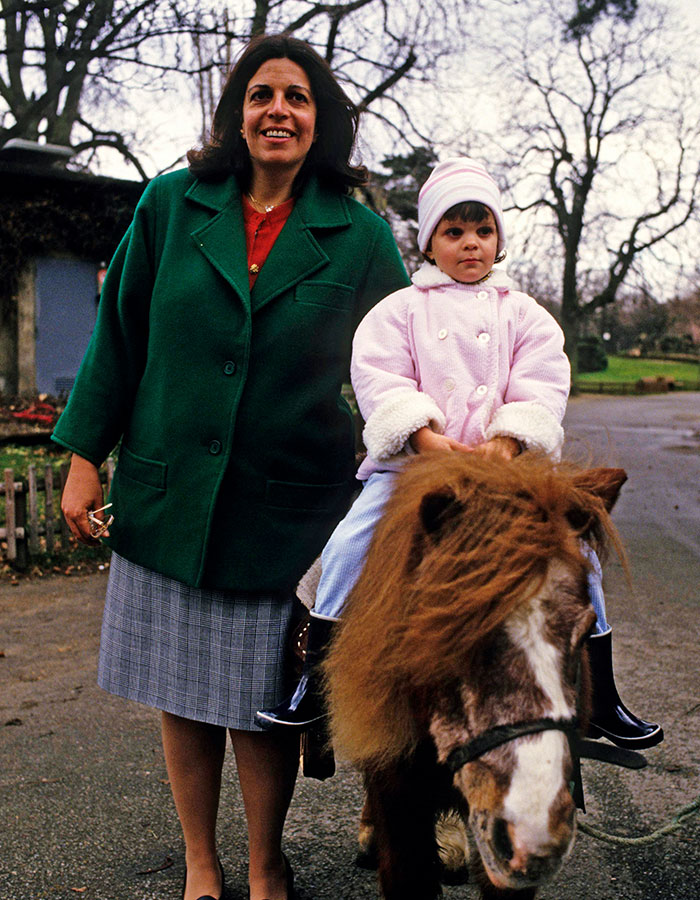 Woman standing next to a child riding a pony outdoors, highlighting reclusive billionaire Athina Onassis in rare appearance.