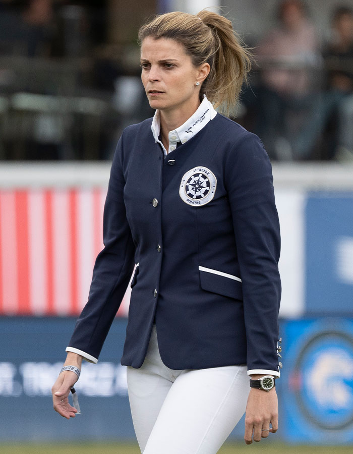 Athina Onassis wearing a navy blazer and white pants, making a rare appearance in a sports event after years in seclusion