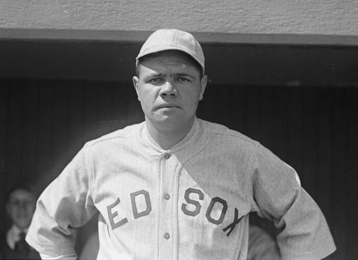 Baseball player in vintage Red Sox uniform and cap standing with arms on hips illustrating from poverty to super wealthy.