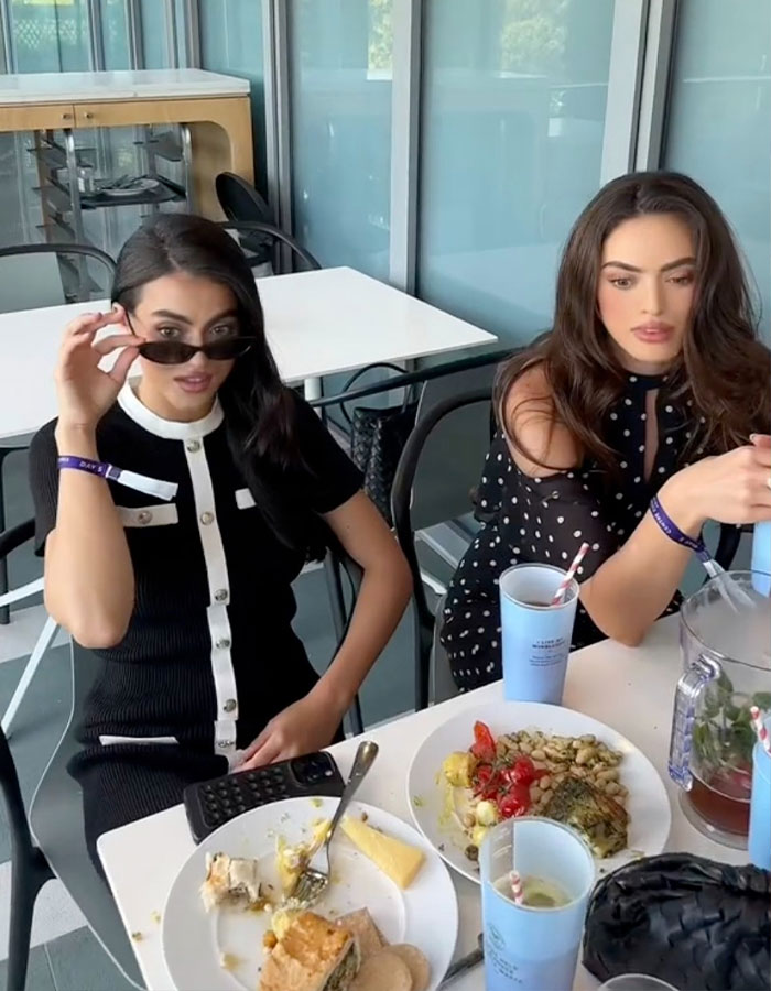 Two women sitting at a table with food and drinks, highlighting Brooks Nader praised for normalizing period leaks.