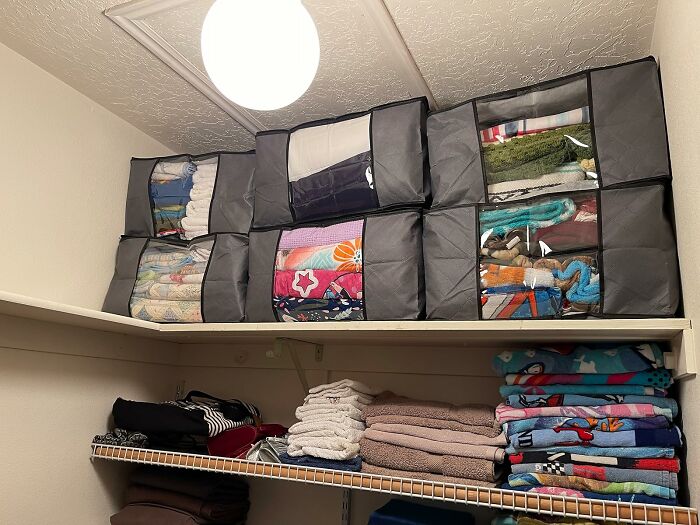 Stacked fabric storage bins neatly organizing linens and towels in a closet, showcasing clever products to organize chaotic home corners.