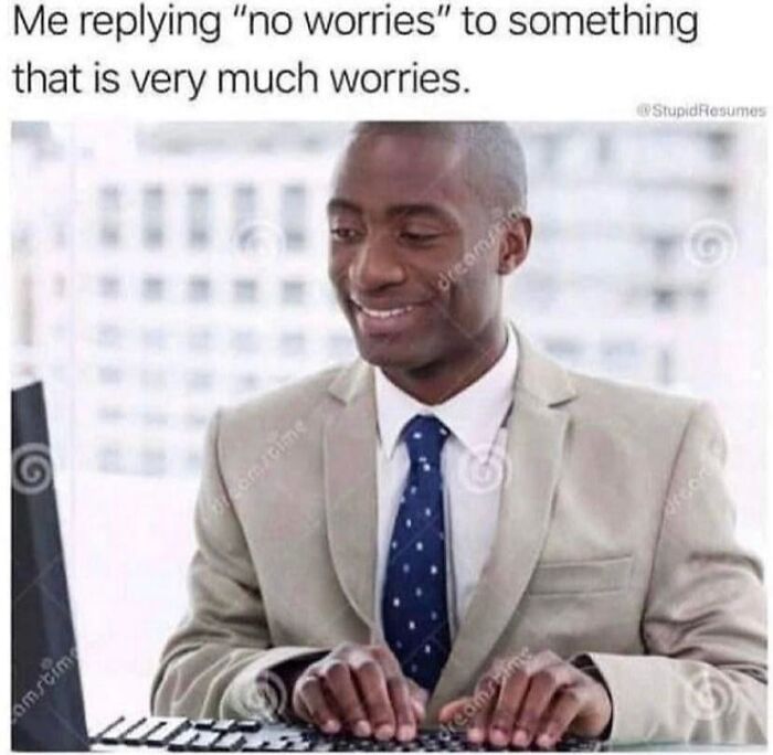 Man in beige suit smiling awkwardly while typing on keyboard, humorously expressing social anxiety memes feeling worried inside.