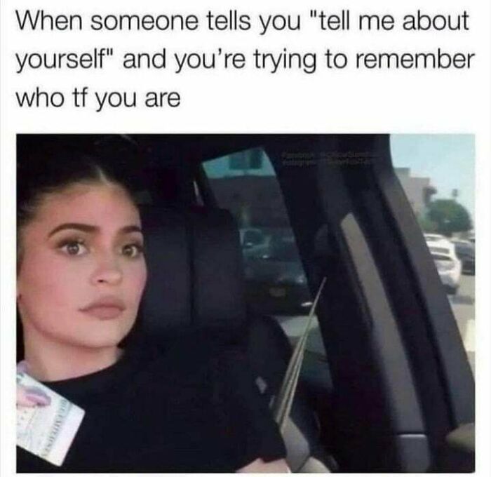Woman sitting in a car with a blank expression, humorously depicting social anxiety memes about identity and self-awareness.