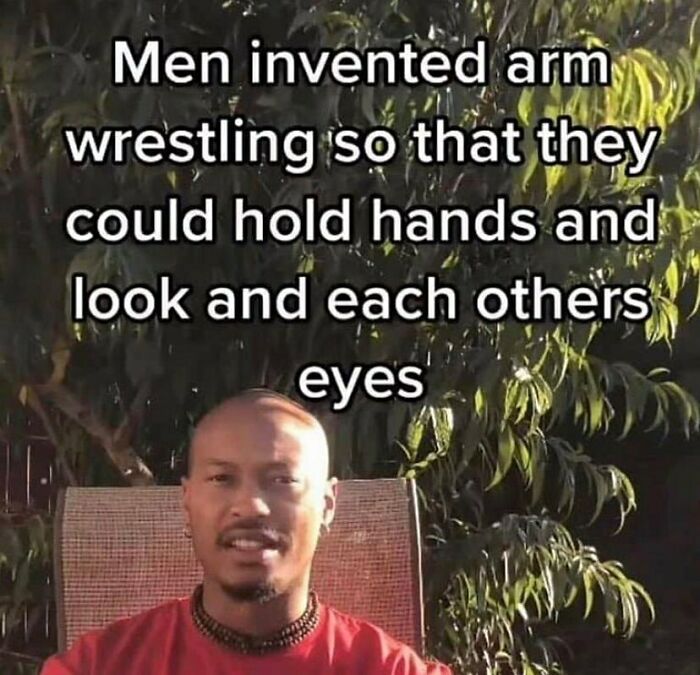 Man sitting outdoors with text about men inventing arm wrestling to hold hands, related to LGBTQ+ memes content.