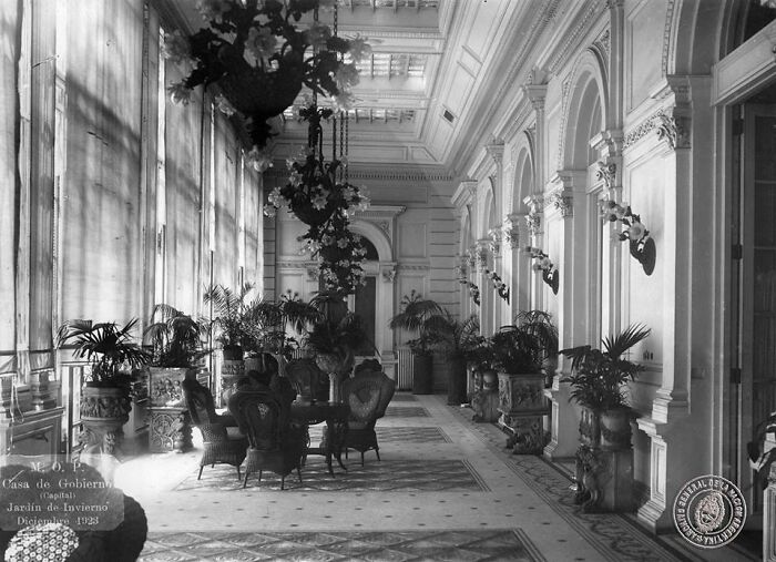 Interior view of a historical government building with ornate furniture and plants in a photograph from 100 years ago.