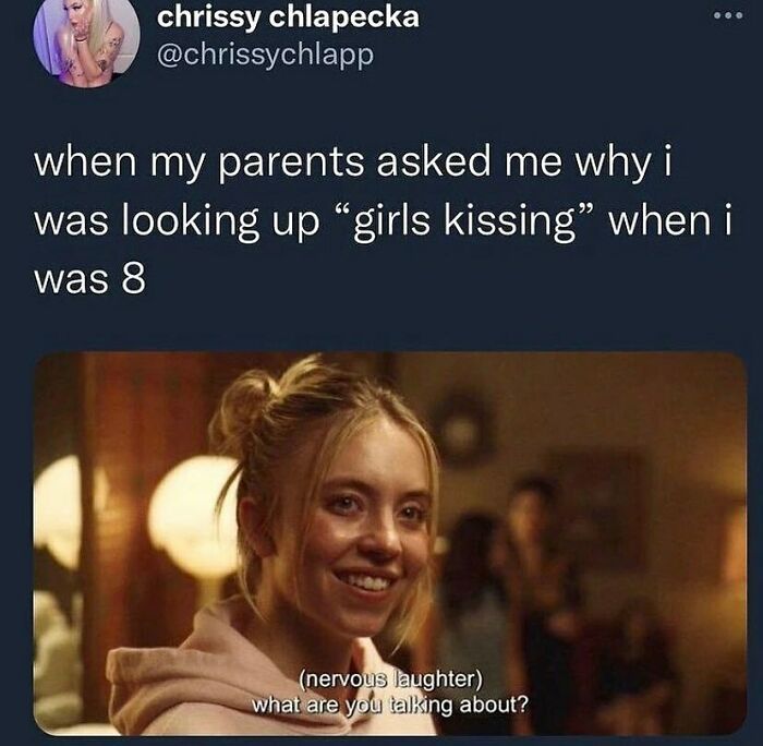 A screenshot of an LGBTQ+ meme with a nervous girl smiling, referencing childhood curiosity about girls kissing.
