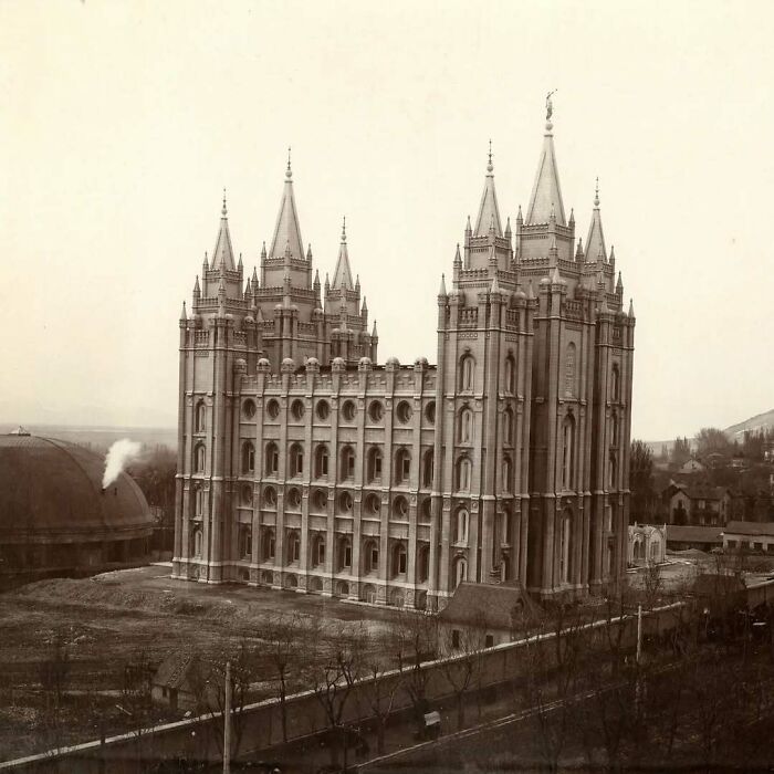 Historic old architecture of a large gothic-style building with multiple spires and detailed stonework in a vintage setting.