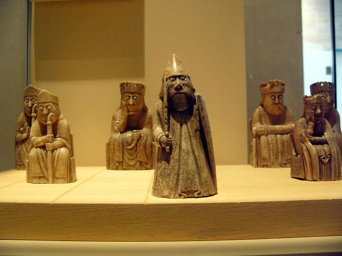 Chess pieces made of carved ivory displayed as foreign artifacts held in the British Museum on a wooden platform.