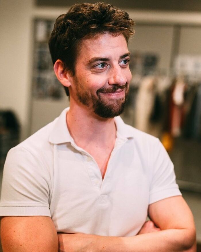 Man with a beard smiling and looking to the side, caption related to Hugh Jackman and Sutton Foster closeness.