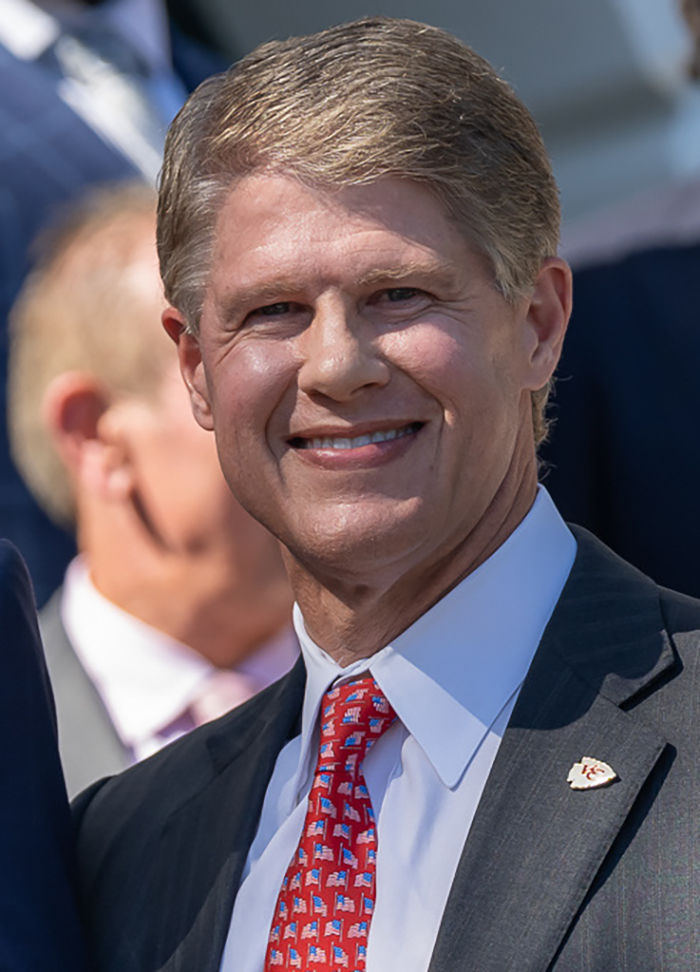 Man in suit and red patterned tie smiling outdoors, related to family of Travis Kelce's boss and Texas floods tragedy.
