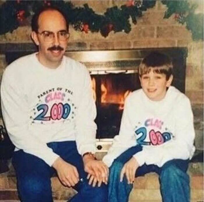 Father and son from the past wearing matching Class of 2000 sweatshirts, sitting by a fireplace showing old school cool style.