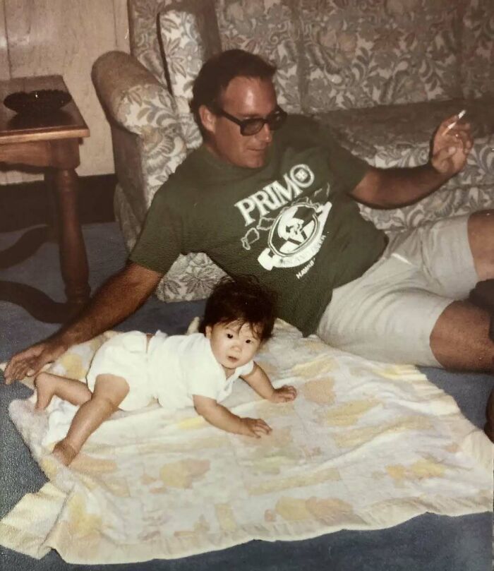 Vintage photo of a dad embodying old school cool, relaxing with his baby on a blanket indoors.