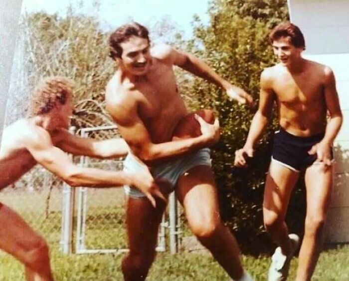 Vintage photo of dads playing football shirtless outdoors, showcasing old school cool style and active lifestyle.