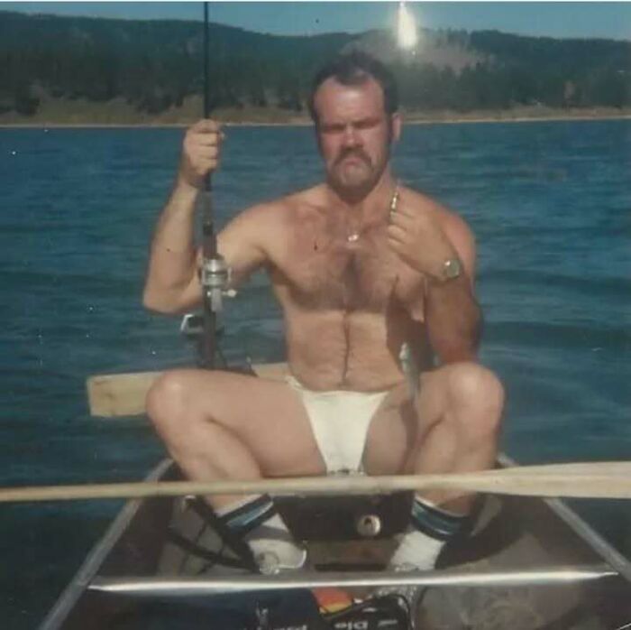 Shirtless dad fishing on a boat wearing white briefs and striped socks, embodying old school cool vibes outdoors.