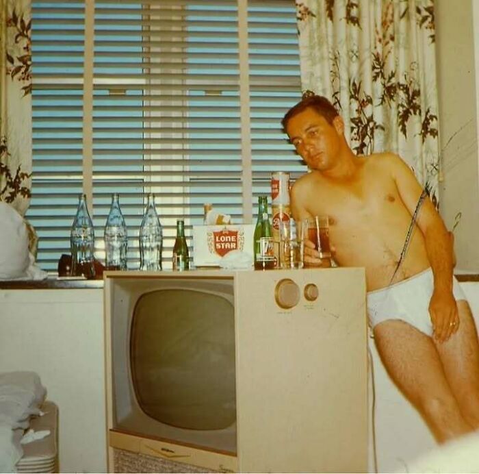Shirtless dad leaning on vintage TV with drinks and Lone Star beer in a retro room, showing old school cool dad style.