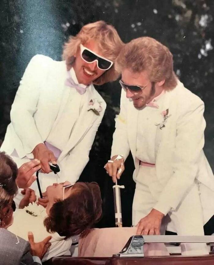 Two dads from the past in white suits and sunglasses showing old school cool while having fun at a party.