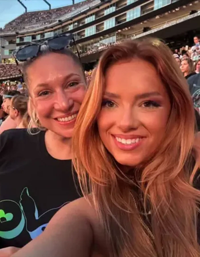Two smiling women at a Coldplay concert, one wearing sunglasses, with a large crowd and stadium background.