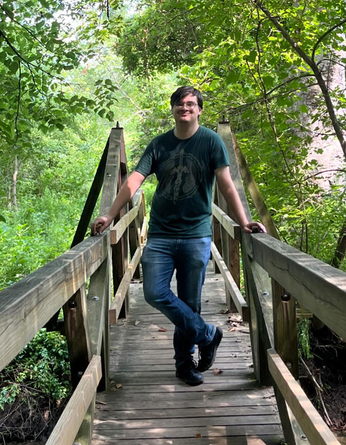 Young man standing on a wooden bridge surrounded by greenery, related to conjoined twin influencer wedding surprise.