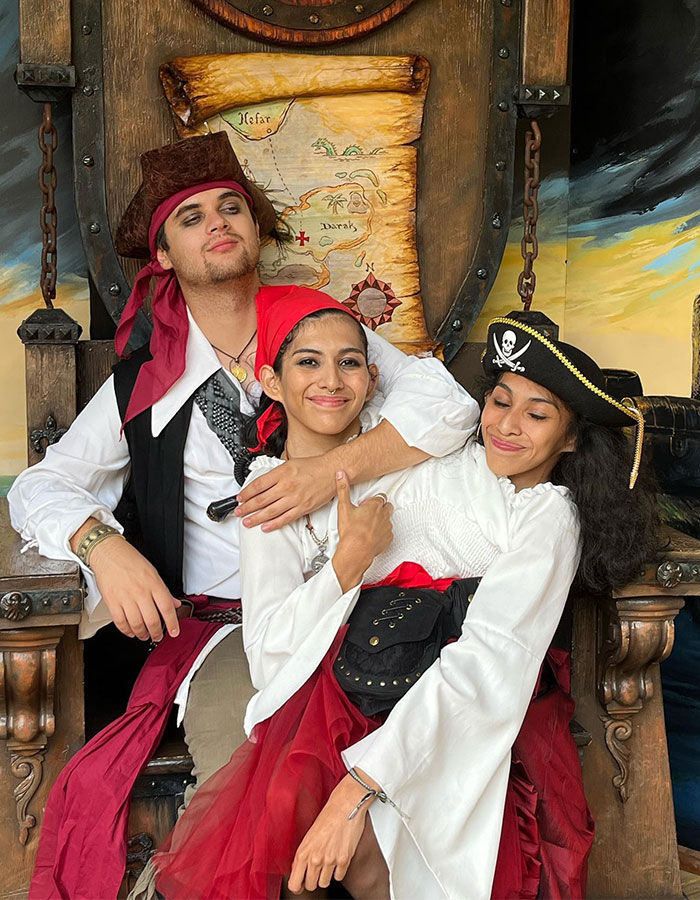 Conjoined twin influencer smiling with friends dressed as pirates, celebrating in an intimate themed ceremony setting