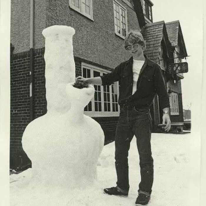 Young man posing with a tall, old school cool snowman outside a house in a vintage black and white photo.