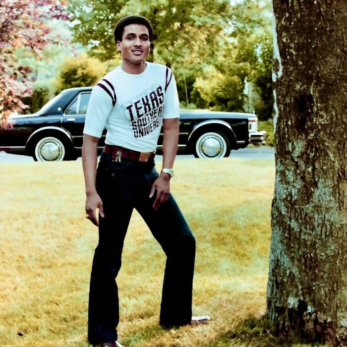 Young man embodying old school cool, wearing a Texas Southern University shirt, standing outdoors near a vintage car.