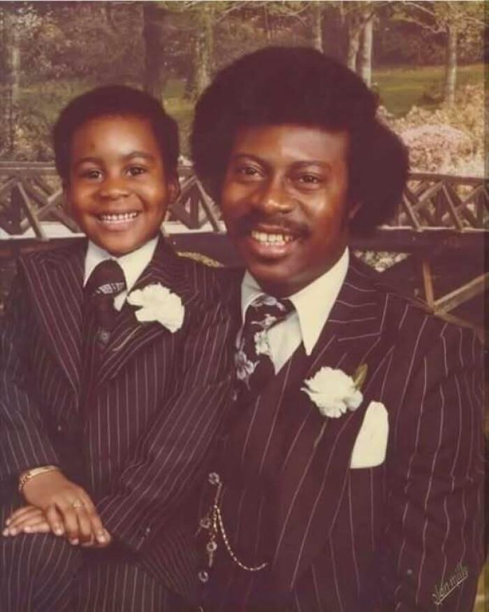 Father and son dressed in matching suits smiling outdoors, representing classic old school cool style from the past.