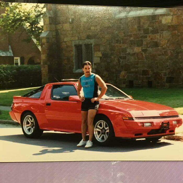Man posing next to a red sports car in vintage athletic wear, showcasing old school cool dad style from the past.