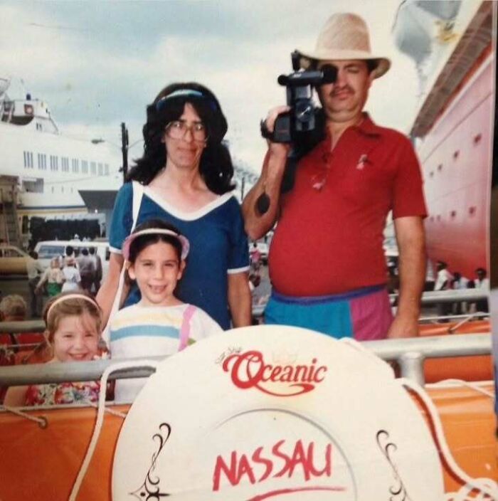 Vintage dad wearing hat filming with camcorder by a ship, accompanied by family in a nostalgic old school cool setting.
