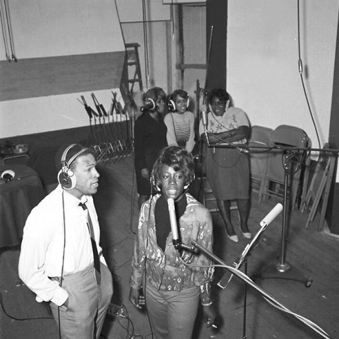 1970s rock legends working together in a vintage recording studio wearing headphones and singing into microphones.