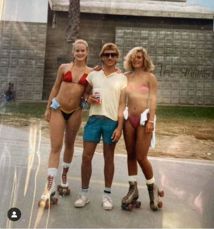 Man with mustache and sunglasses in vintage outfit standing between two women in bikinis and roller skates, old school cool dads.