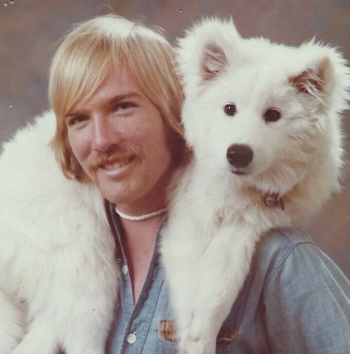 Retro dad with blonde hair and mustache posing with a fluffy white dog on his shoulders, showcasing old school cool style.