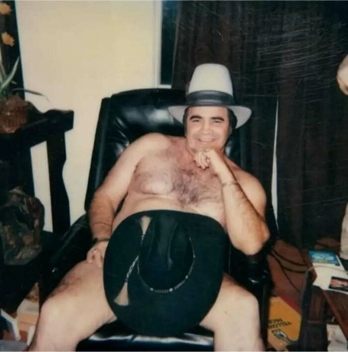Shirtless old school cool dad wearing two hats, reclining confidently in a leather chair with a relaxed smile.