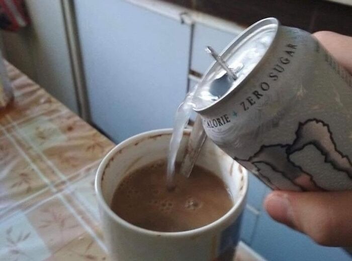 Energy drink being poured into a coffee mug with coffee inside, a funny gym meme about workout habits.