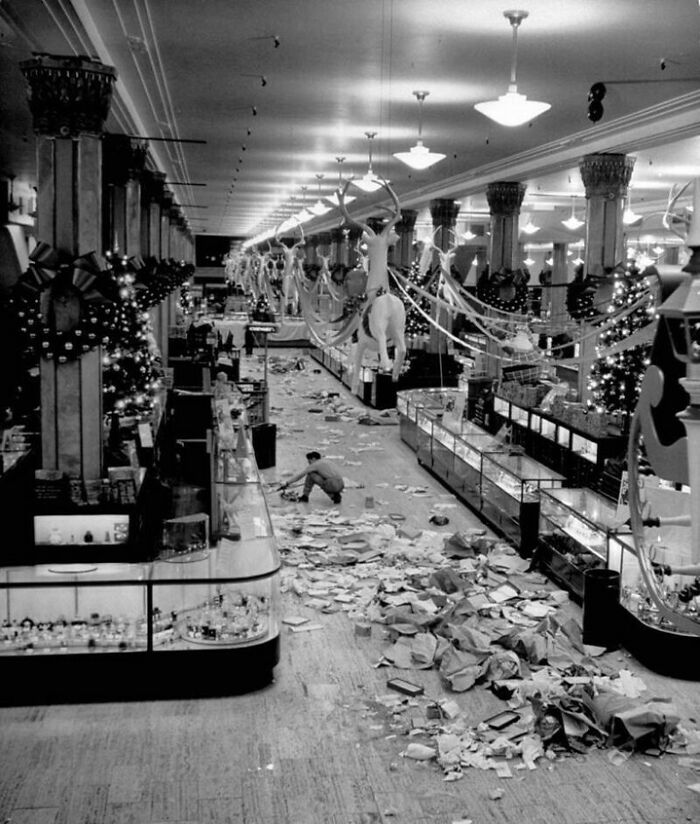 Black and white photo of a large department store with holiday decorations and scattered papers on the floor, interesting facts.