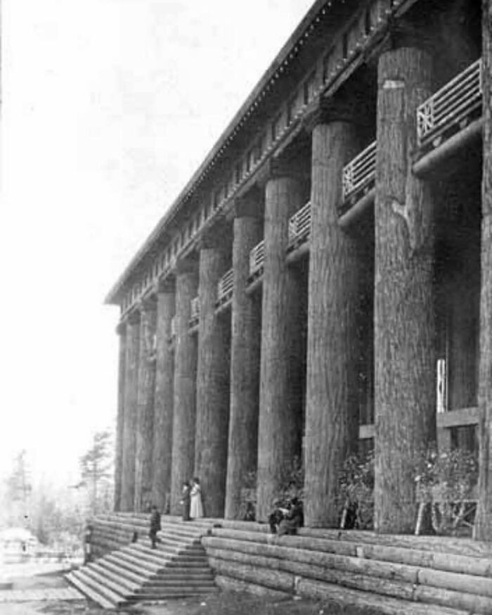 Old architecture featuring large wooden columns and steps with people gathered around the historic building facade.