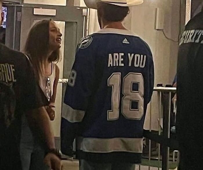 Person wearing a jersey with text "ARE YOU 18" in a dimly lit environment, one of the pics that make no sense at all.