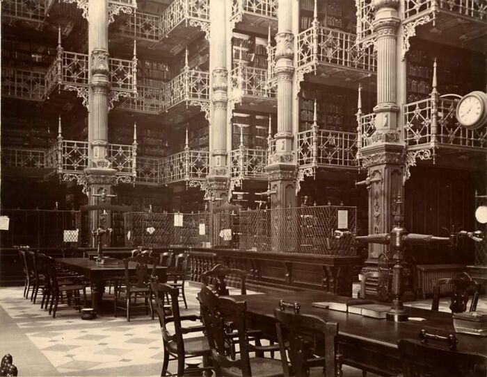 Victorian old architecture interior with ornate columns, metal railings, and wooden tables in a historic library setting.