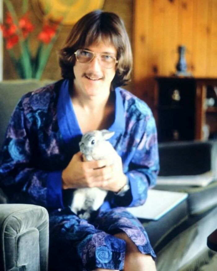 Man in vintage old school cool outfit holding a rabbit, sitting in a retro living room setting from the past.