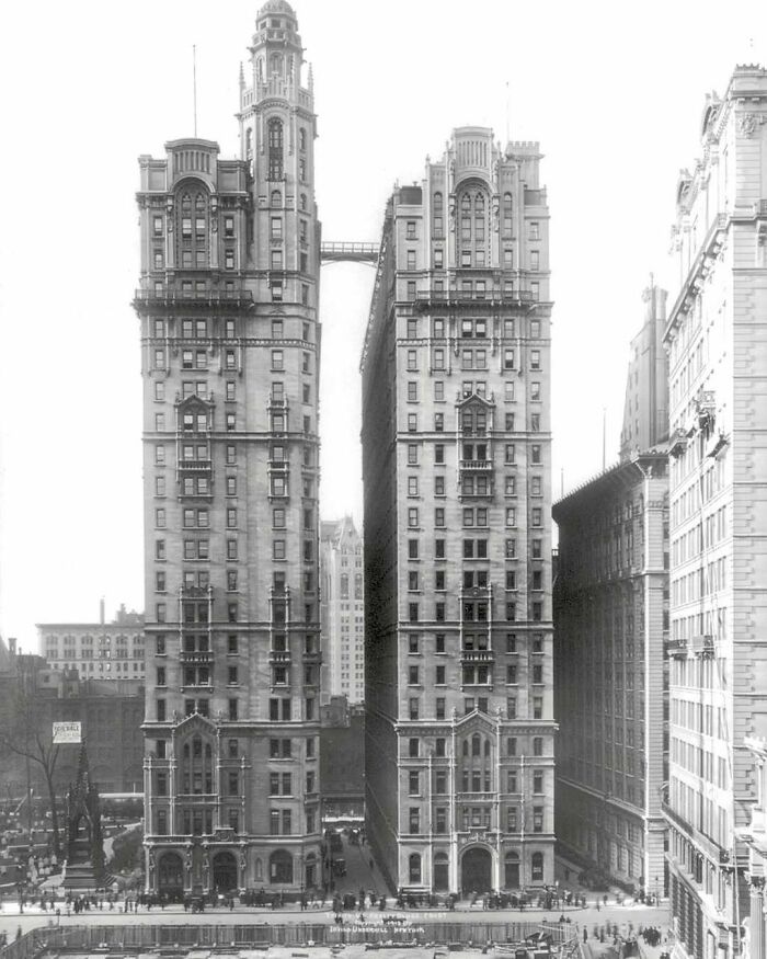 Black and white photo of old architecture showing two historic high-rise buildings connected by a skybridge in a cityscape.