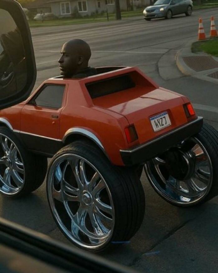 Man driving a small car with oversized shiny rims, creating a bizarre scene that makes no sense but draws attention.