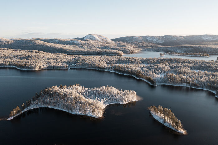 Aerial view of a snowy forested cabin in the woods surrounded by a calm lake, depicting a peaceful true home retreat. - 2