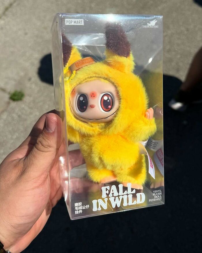 Hand holding a creepy yellow Labubus fake doll in clear packaging labeled Fall In Wild vinyl plush pendant.
