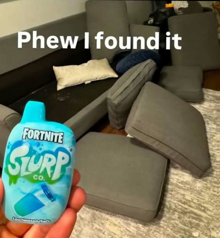 Hand holding Fortnite Slurp drink in front of a couch with scattered cushions in a bizarre room setting.