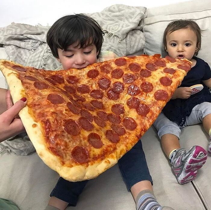 Child eating an oversized slice of pepperoni pizza, surprising size contrast making no sense but captivating to look at
