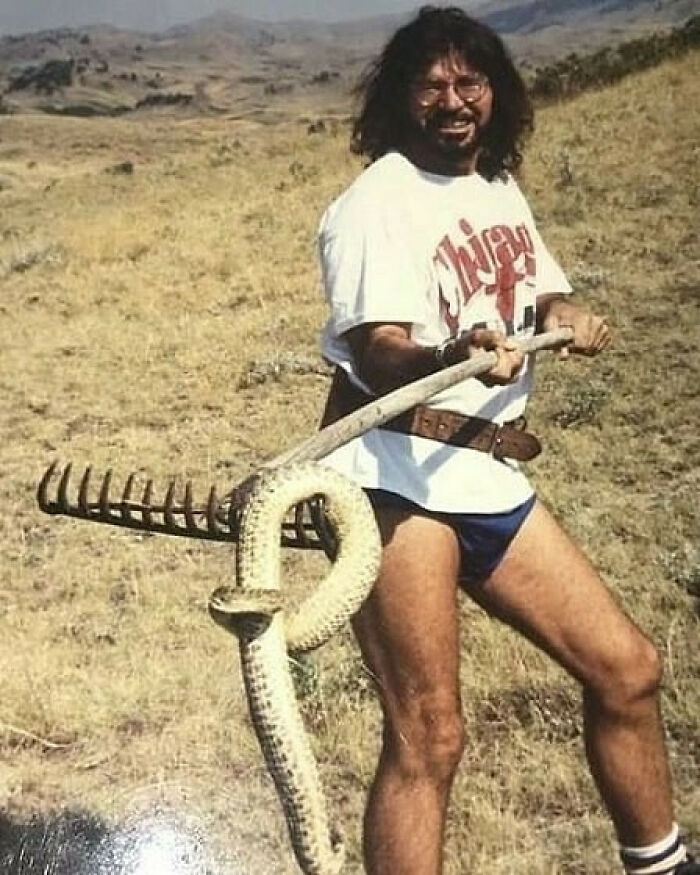 Man from the past wearing shorts holding a rake with a snake wrapped around it, embodying old school cool dads style.